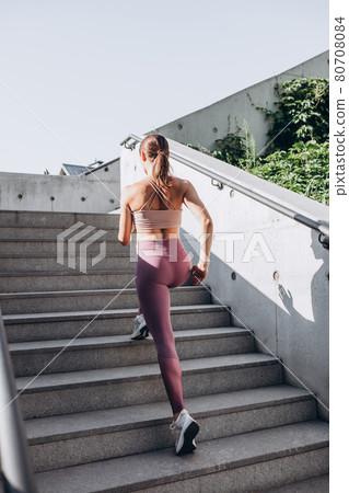 Back view. Young slim sportive caucasian woman working out, doing fitness, yoga on the stairs on city street. Back view. Young slim sportive caucasian woman working out, doing fitness, yoga on the stairs on city street. 80708084