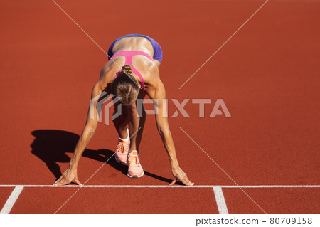 At start line. One Caucasian woman, female athlete, runner training at public stadium, sport court or palyground outdoors. Summer sport games. At start line. One Caucasian woman, female athlete, runner training at public stadium, sport court or palyground outdoors. Summer sport games. 80709158