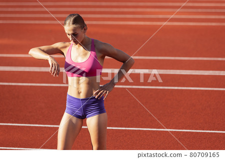 One Caucasian woman, female athlete, runner training at public stadium, sport court or palyground outdoors. Summer sport games. 80709165