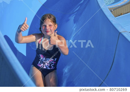 Pretty litlle girl sliding on water slide. Funny children's attraction at water park. Vacation concept Pretty litlle girl sliding on water slide. Funny children's attraction at water park. Vacation concept 80710269