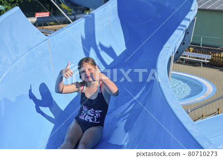 Girl sliding down on a water slide in aqua park. Vacation concept. Holiday fun Girl sliding down on a water slide in aqua park. Vacation concept. Holiday fun 80710273