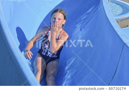 Girl sliding down on a water slide in aqua park. Vacation concept. Holiday fun 80710274