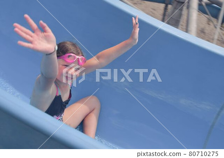 Girl sliding down on a water slide in aqua park. Vacation concept. Holiday fun Girl sliding down on a water slide in aqua park. Vacation concept. Holiday fun 80710275