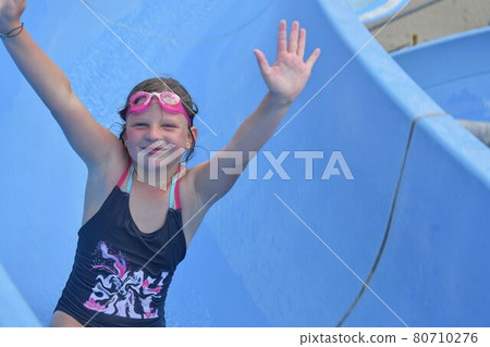 Girl sliding down on a water slide in aqua park. Vacation concept. Holiday fun Girl sliding down on a water slide in aqua park. Vacation concept. Holiday fun 80710276