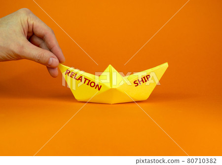 Image of businessman pushing paper made origami boat forward in a conceptual image. Words 'relation ship'. Over orange background with copy space. Business and relationship concept. Image of businessman pushing paper made origami boat forward in a conceptual image. Words 'relation ship'. Over orange background with copy space. Business and relationship concept. 80710382