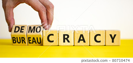 Democracy or bureaucracy symbol. Businessman turns wooden cubes and changes the word bureaucracy to democracy. Beautiful white background, copy space. Business and democracy or bureaucracy concept. 80710474