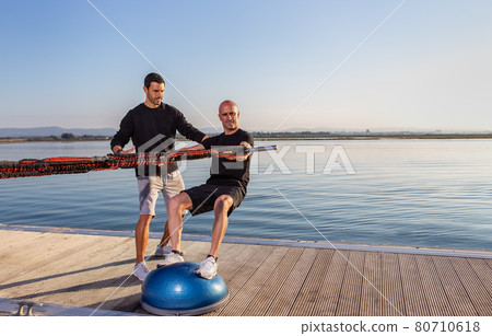 A windsurfer on a stabilization ball stimulates riding on a board with rubber expanders. To develop equilibrium and stability. A windsurfer on a stabilization ball stimulates riding on a board with rubber expanders. To develop equilibrium and stability. 80710618