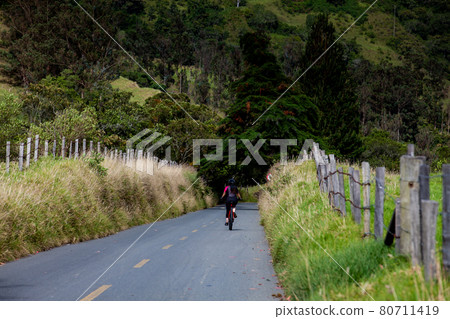 Woman riding her bike on the beautiful landscapes of the Cocora Valley located at the Quindio region in Colombia 80711419