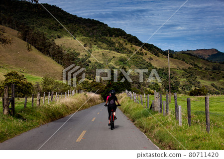 Woman riding her bike on the beautiful landscapes of the Cocora Valley located at the Quindio region in Colombia 80711420