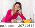 Woman leaning on the table having breakfast cereal with fruit and milk while talking on the phone 80711649