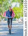Smiling latino man wrapped in USA flag riding an electric scooter: Selective focus. Diversity concept. 80711650