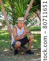 Latino man playing the trumpet crouched near a plant outdoors 80711651
