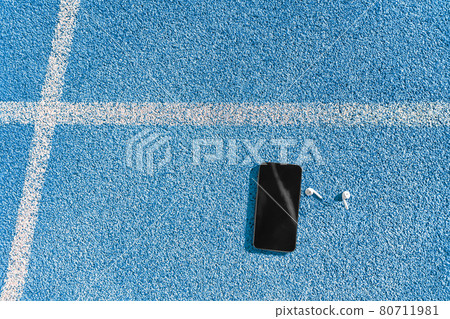 Running track and field lane and smartphone for music listening on mobile phone app with earphones earbuds. Blue background texture of tracks lanes for copyspace for fitness and sports concepts 80711981