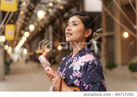 A woman in a yukata cooling off with a mini electric fan (handy fan) in the evening shopping district at Endoji Shopping District 80717202