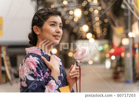 A woman in a yukata cooling off with a mini electric fan (handy fan) in the evening shopping district at Endoji Shopping District 80717203