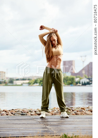 A beautiful woman, blonde, fitness instructor, in light clothes, trains on the beach, against the backdrop of the city. Shows exercises from yoga, pilates, deep work, step aerobics. A beautiful woman, blonde, fitness instructor, in light clothes, trains on the beach, against the backdrop of the city. Shows exercises from yoga, pilates, deep work, step aerobics. 80718475
