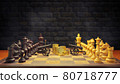 Chess and cannon are facing each other on chessboard with gold coin in between them and smoke floating in the air and dark brick background. The concept of business battles. 80718777