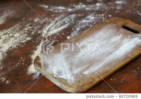A kitchen table with a wooden cutting board is covered in flour. A kitchen table with a wooden cutting board is covered in flour. 80720908