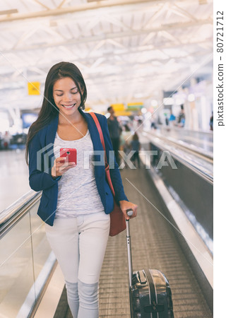 Travel airport Asian woman using mobile phone walking with suitcase on moving walkway in terminal on business trip. Technology wifi online in lounge. Air travel lifestyle 80721712