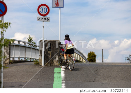 Summer girl climbing a slope with a bridge by bicycle 80722344