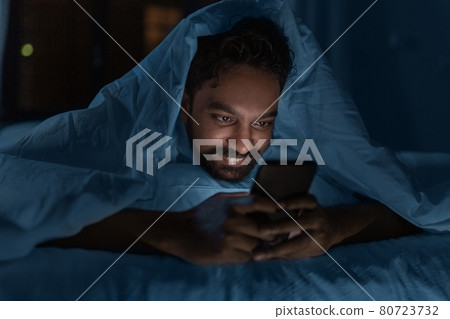 indian man with smartphone in bed at home at night indian man with smartphone in bed at home at night 80723732