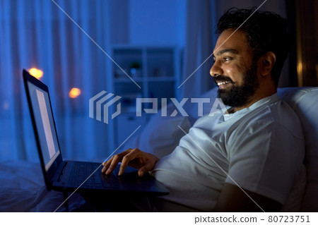 indian man with laptop in bed at home at night indian man with laptop in bed at home at night 80723751
