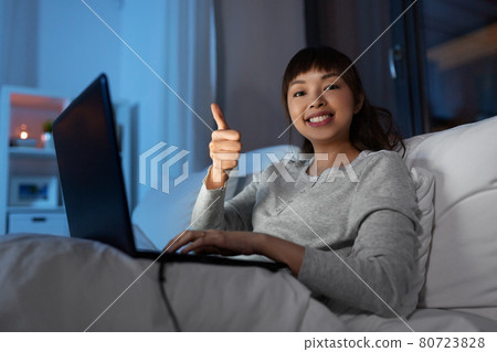 woman with laptop in bed at night shows thumbs up woman with laptop in bed at night shows thumbs up 80723828