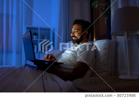 indian man with laptop in bed at home at night 80723986