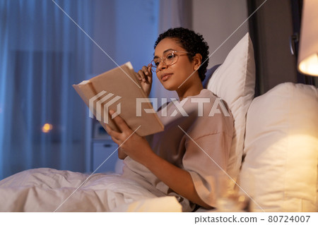 young woman in glasses reading book in bed at home young woman in glasses reading book in bed at home 80724007