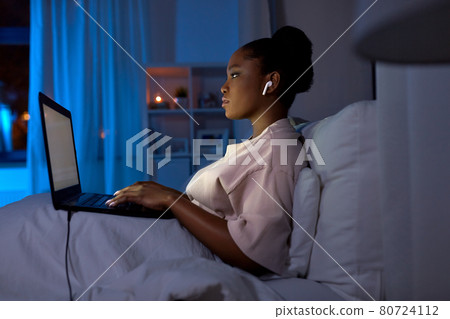 woman with laptop and earphones in bed at night woman with laptop and earphones in bed at night 80724112
