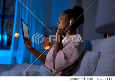woman with tablet pc in earphones in bed at night 80724114