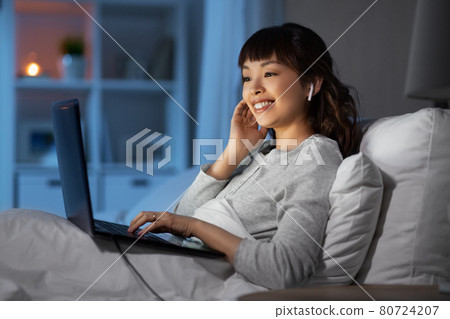 woman with laptop and earphones in bed at night woman with laptop and earphones in bed at night 80724207