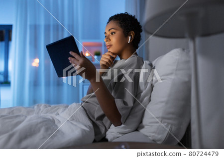 woman with tablet pc in earphones in bed at night 80724479