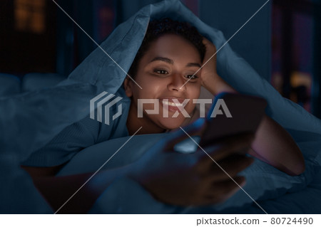 woman with smartphone under duvet in bed at night woman with smartphone under duvet in bed at night 80724490