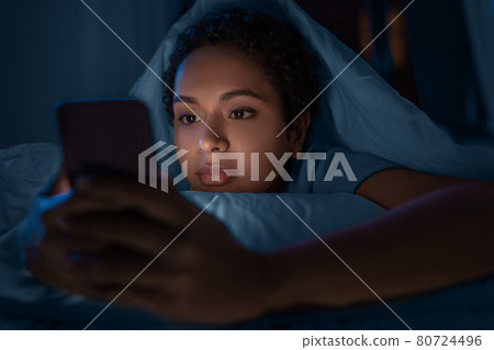 woman with smartphone under duvet in bed at night woman with smartphone under duvet in bed at night 80724496