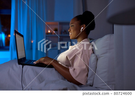 woman with laptop and earphones in bed at night woman with laptop and earphones in bed at night 80724600