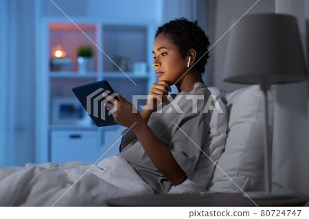 woman with tablet pc in earphones in bed at night 80724747