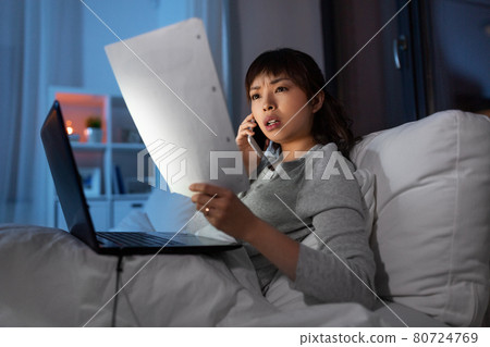 woman with laptop calling on phone in bed at night woman with laptop calling on phone in bed at night 80724769
