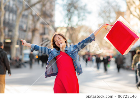 Autumn fashion sale happy woman walking with shopping bags on La Rambla street in Barcelona. Shopper Asian girl ecstatic with open arms holding purchases excited 80725146