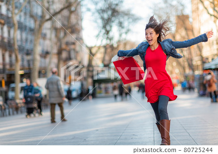 Happy Asian woman walking with shopping bags on Barcelona, La Rambla street. Shopper with open arms up enjoying sale. From tourist destination in Catalonia, Spain travel 80725244