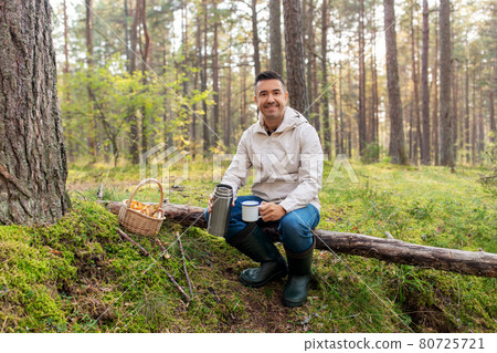 man with basket of mushrooms drinks tea in forest 80725721
