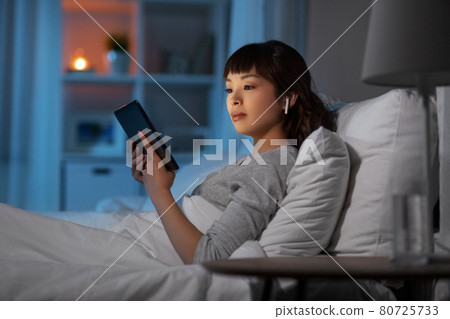 woman with tablet pc in earphones in bed at night woman with tablet pc in earphones in bed at night 80725733