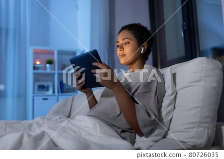 woman with tablet pc in earphones in bed at night woman with tablet pc in earphones in bed at night 80726035