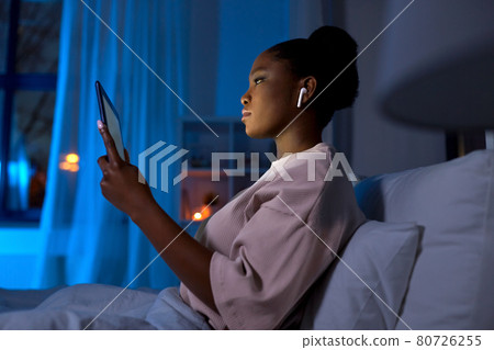 woman with tablet pc in earphones in bed at night woman with tablet pc in earphones in bed at night 80726255
