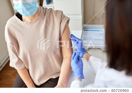 female doctor with syringe vaccinating patient 80726960