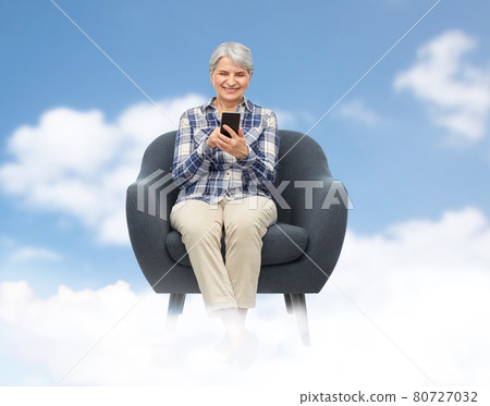 smiling senior woman with smartphone in chair smiling senior woman with smartphone in chair 80727032