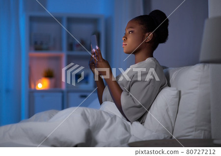 woman with smartphone in bed at home at night woman with smartphone in bed at home at night 80727212