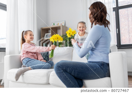 daughters giving daffodil flowers to happy mother 80727467