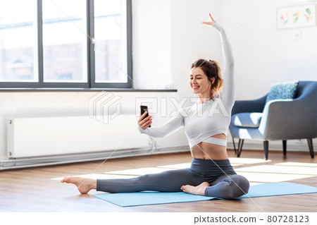 young woman with smartphone doing yoga at home young woman with smartphone doing yoga at home 80728123