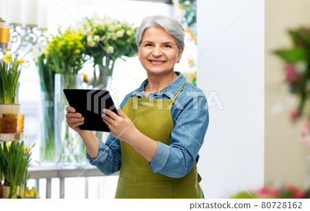 happy senior woman in garden apron with tablet pc 80728162